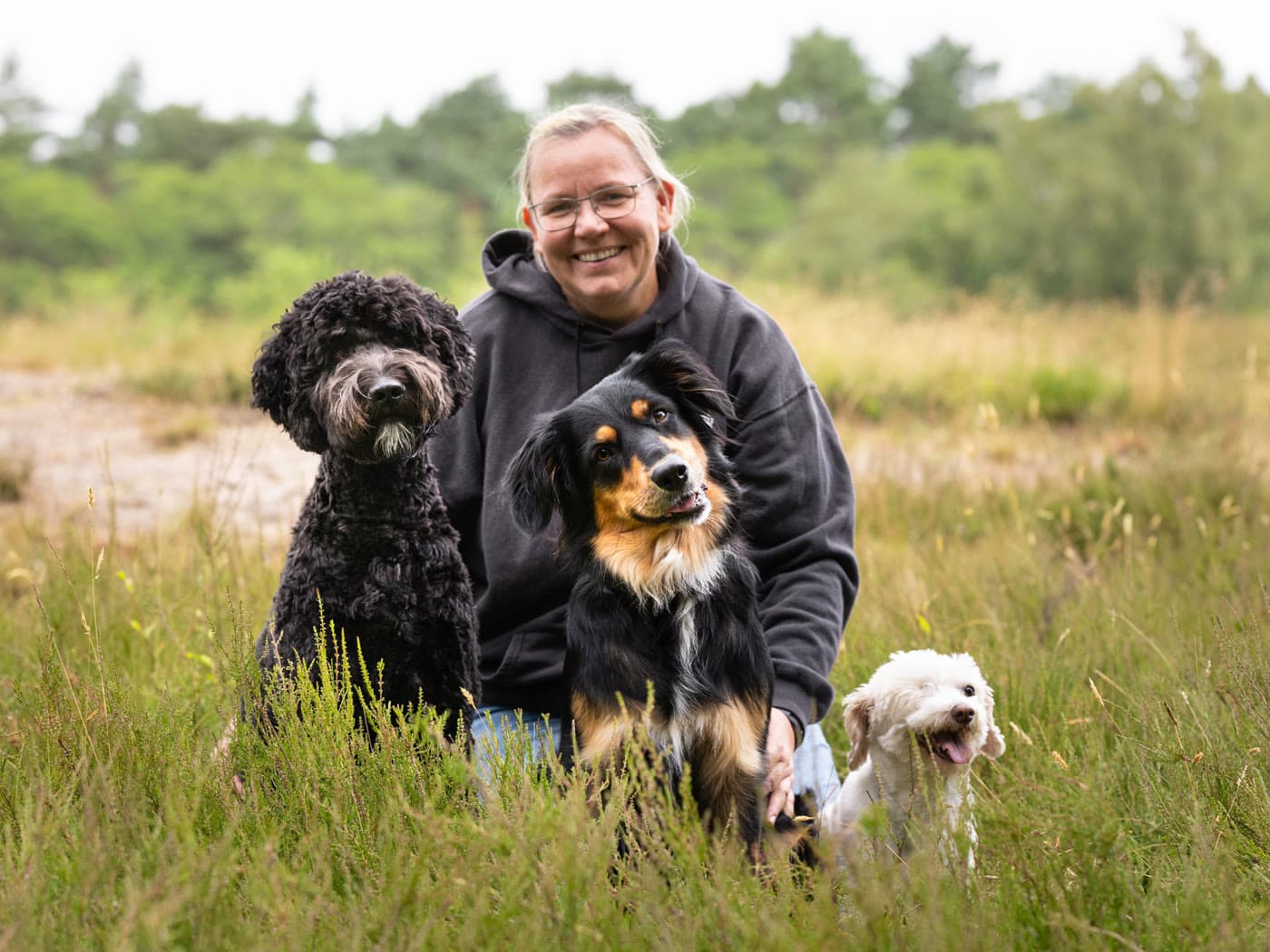 Martina Garske kniet lächelnd zwischen ihren drei Hunden in der Heide